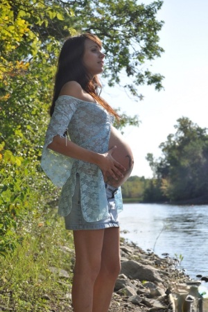 Solo girl Brianna exposes her pregnant belly on rocky shore beside a river