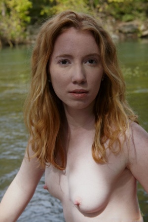Young redhead Nicki Blue bare her small tits while standing in a stream