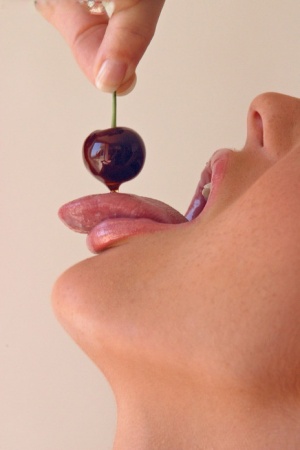 Pretty girl Sandra Shine curls her tongue while sucking juice from a cherry