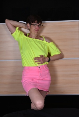 Mature woman undoes the snap and zipper on a pink miniskirt during SFW action