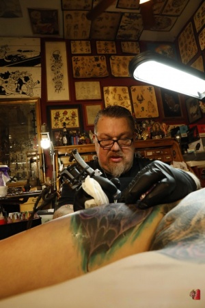 Naked brunette Marie Bossette lies on her back while getting a new tattoo