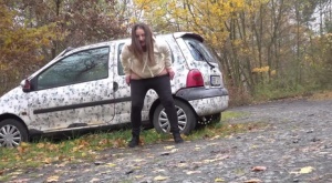 White girl Nicolette Noir takes a piss beside a parked car in a wooded setting