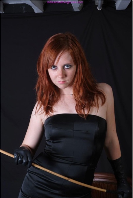 Natural redhead holds a cane with leather gloves while exposing her pink slit