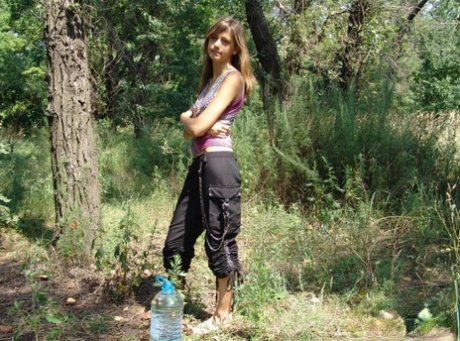 Young amateur drinks from a jug of water while barefoot in the woods 38281462