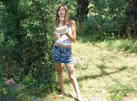 Cute young girl in denim skirt undressing outdoors to smear food on her body 57193176