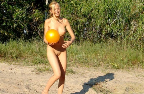 Blonde teen holds a ball while posing totally nude on a patch of sand 88529082