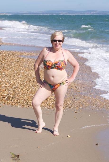 Mature UK woman Speedy Bee wears sunglasses while getting naked at the beach 25573663