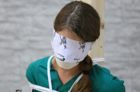 Caucasian nurse is blindfolded and gagged while tied to a wooden post 37466705