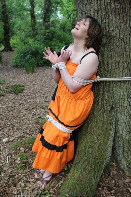Fat female is gagged and tied to a tree in the woods with her clothes on 62870170