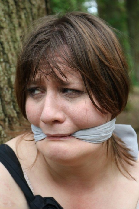 Fat female is gagged and tied to a tree in the woods with her clothes on 62870170