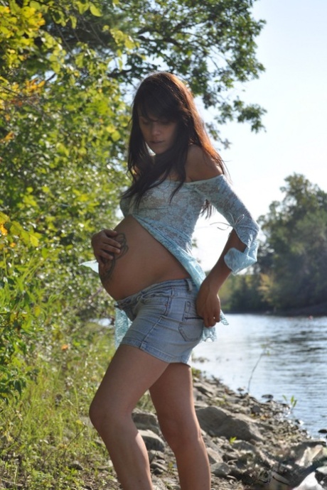 Solo girl Brianna exposes her pregnant belly on rocky shore beside a river 99676339