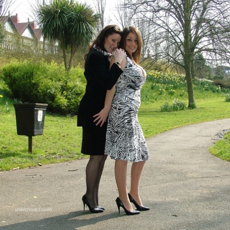 Clothed ladies hold hands while showing their spiked heels on a walking path 60998577