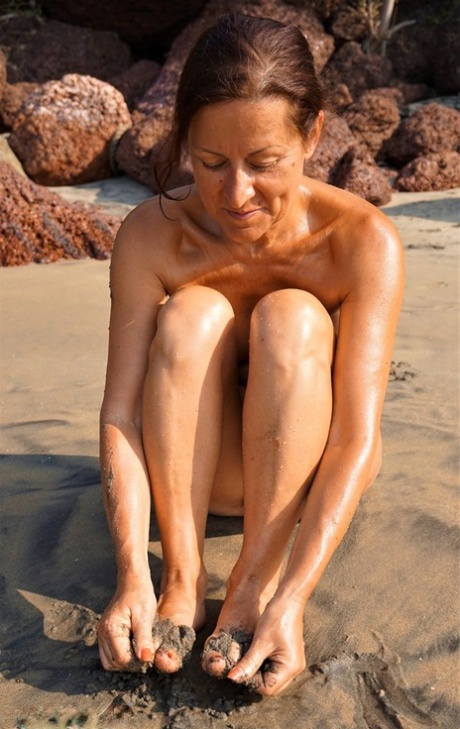 Naked older woman Diana Ananta covers her feet in beach sand at low tide 93463451