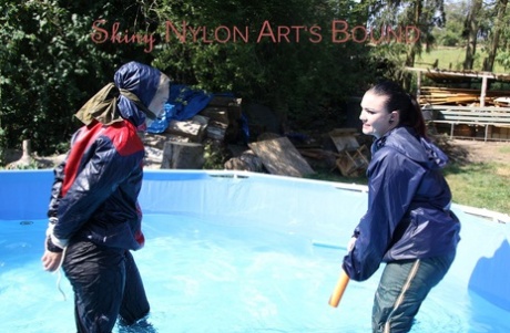 Blonde girl is restrained in rainwear by a lesbian in a backyard pool