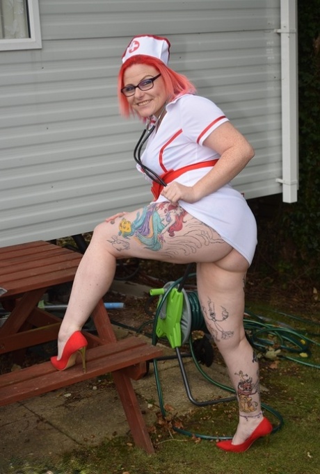 Thick redhead removes leather attire to pose nude before donning nurse garb 15518322