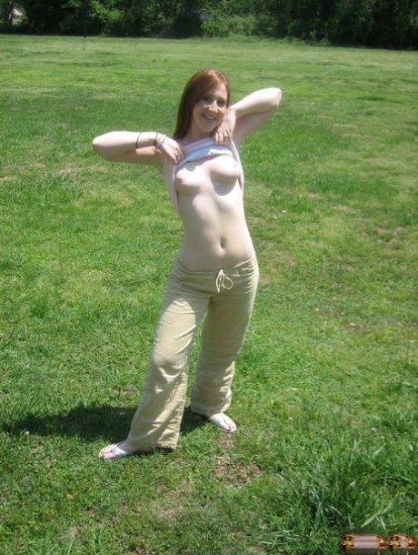 Natural redhead flashes her tits on playground equipment in a field