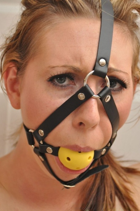 Topless white girl is restrained to a coat rack while ball gagged