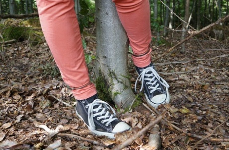 Clothed girl in canvas sneakers finds herself handcuffed to a tree in woods 91552549