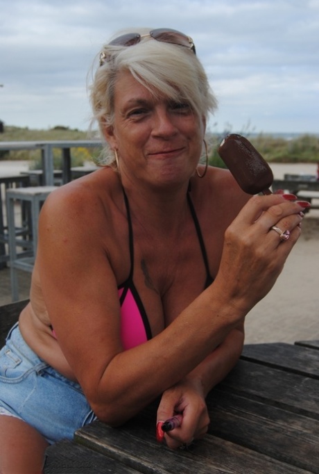 Mature blonde Dimonty eats a frozen treat after posing nude on a beach 56344943