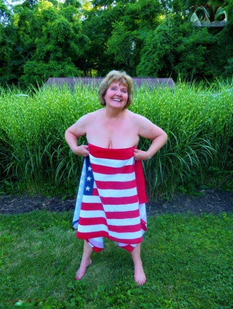 Older plumper Busty Bliss holds an American flag while totally naked in a yard 74405966