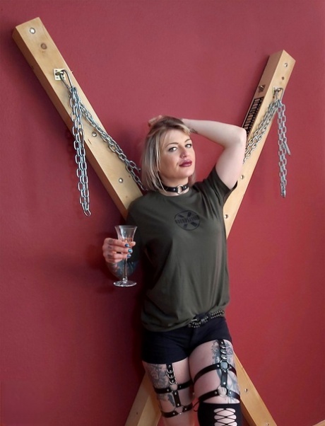 Tatted blonde Roxxxi Manson removes a ball gag in front of a St Andrew's Cross 19497260
