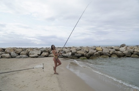 Brunette chick Kitty Angela takes off her bikini while fishing from the shore