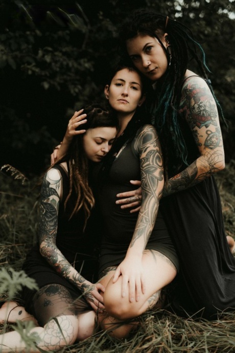 Three tattooed girls share lesbian kisses in long grass near a fir tree 48053646
