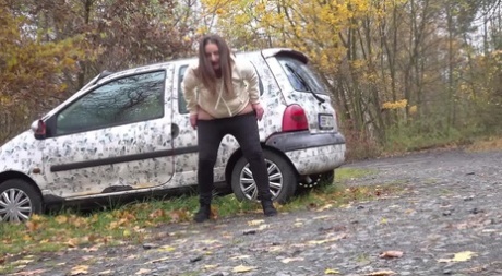 White girl Nicolette Noir takes a piss beside a parked car in a wooded setting