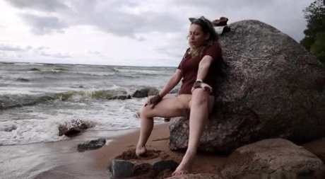 Katy Dee leans back against a boulder on a beach for a badly needed piss