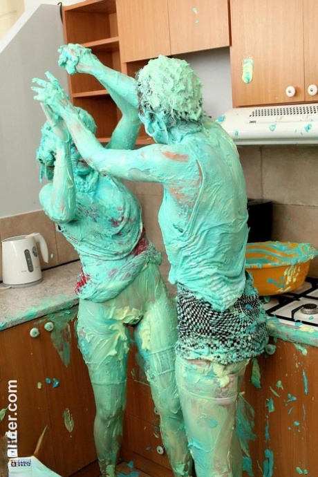 Clothed women cover each other in cake mix during a food fight in kitchen 80255250